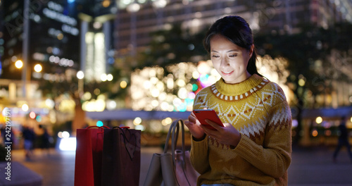 Woman look at mobile phone in city with shopping bag at night