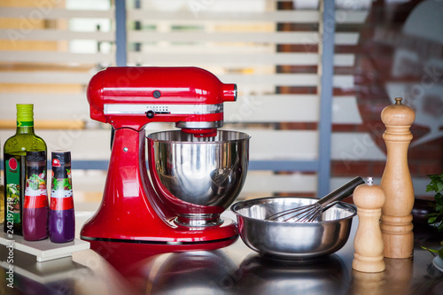 Red professional mixer surrounded by spices and olive oil stands on a metal table