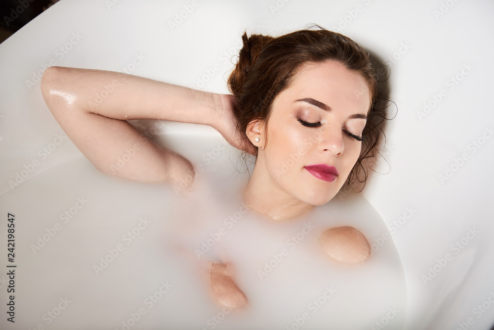 Cute young woman smiling in bath tub full of milk Cute young woman smiling in bath tub full of milk