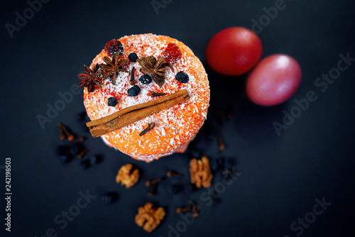 Easter composition of sweet bread decorated with cinnamon, badyan and walnuts, paska, colored red eggs with chokeberry and spices on background. Top view. Delicious fruit cake. Holidays pie photo