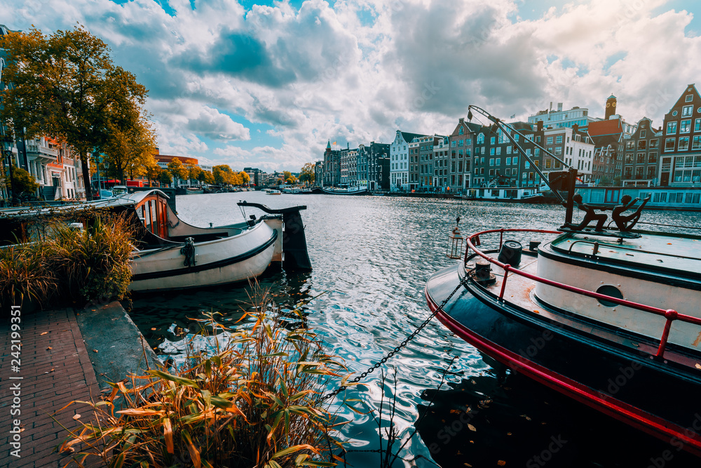 Amsterdam canal Singel with typical dutch houses and houseboats during sunny autumn day. Golden trees and amazing cloudscape. Holland, Netherlands