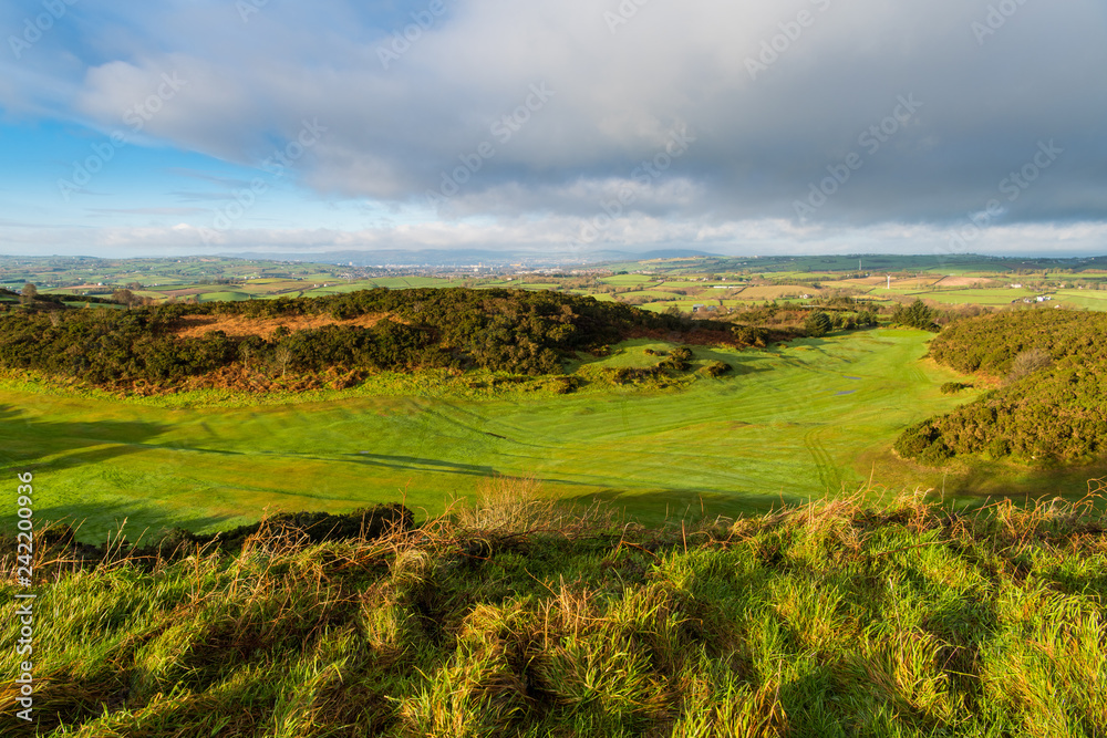 Eary morning golden hour light reveals a lush green golf course with a rolling landscape of grass and fields in the distance on the Ards Peninsula, County Down, Northern Ireland