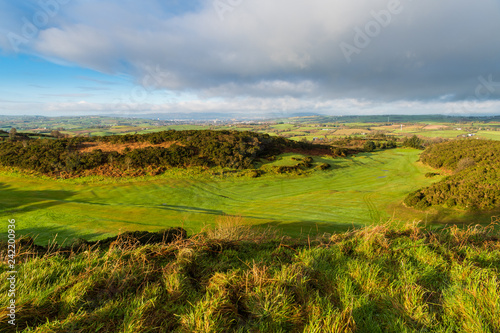 Eary morning golden hour light reveals a lush green golf course with a rolling landscape of grass and fields in the distance on the Ards Peninsula, County Down, Northern Ireland