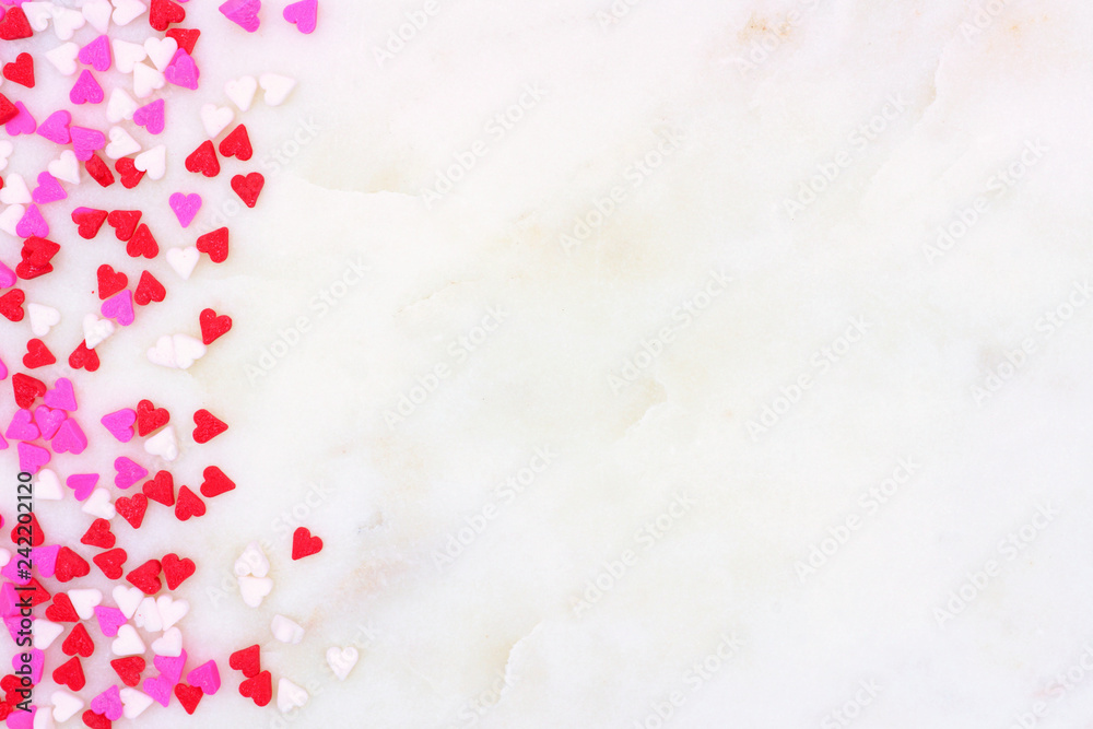 Valentines Day candy heart sprinkles side border over a white marble stone textured background Valentines Day candy heart sprinkles side border over a white marble stone textured background