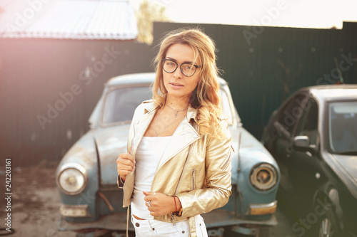 a beautiful blonde with long hair in white denim shorts stands near an old retro car © vadiar