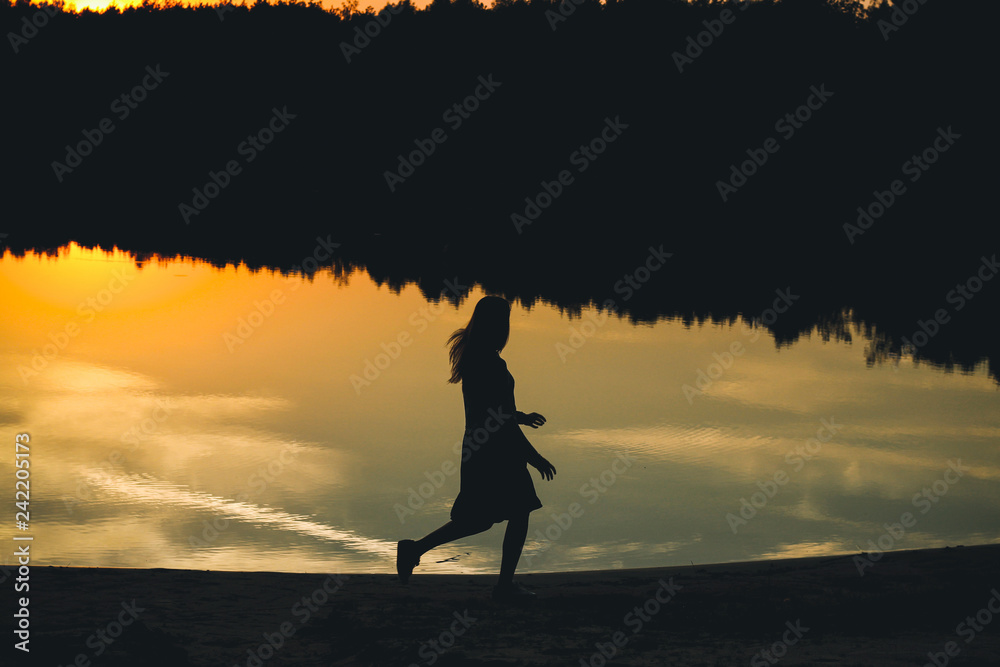 Silhouette of a young beautiful girl on the background of the sunset in the reflection of the pond