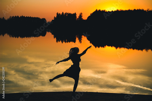 Silhouette of a young beautiful girl in a jump on a background of a sunset in reflection pond