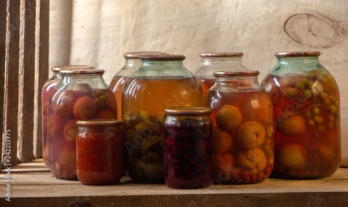 Several cans of compote on a wooden shelf in a dark basement