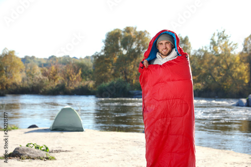Male camper in sleeping bag on wild beach. Space for text