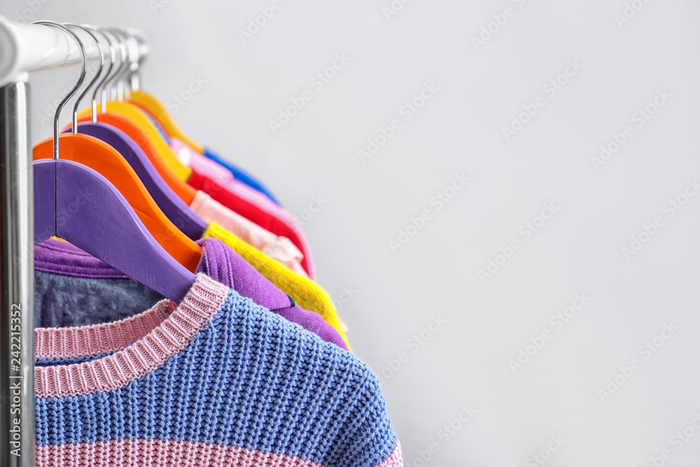 Colorful clothes hanging on wardrobe rack against light background, closeup. Space for text Colorful clothes hanging on wardrobe rack against light background, closeup. Space for text