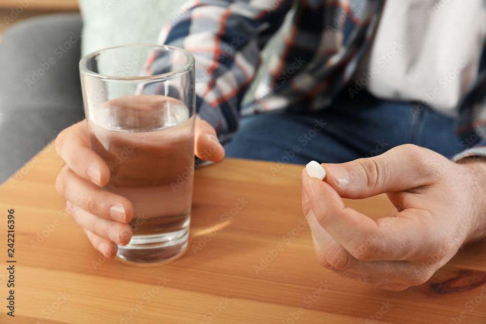 Man holding pill and glass of water at table, closeup Man holding pill and glass of water at table, closeup