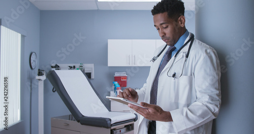 Professional licensed MD using tablet computer inside health clinic. Handsome African-American doctor swiping portable pad in medical room