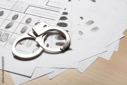 Police handcuffs and criminal fingerprints card on wooden background, space for text