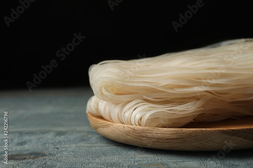 Plate with raw rice noodles on wooden table, closeup. Space for text
