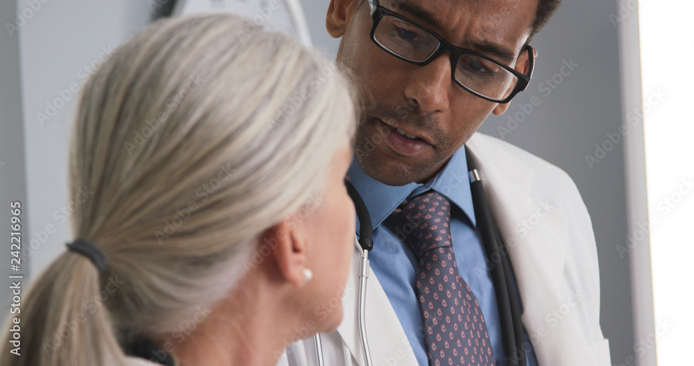 Closeup of two doctors consulting with each other inside medical office. Tight shot of male black doctor talking to senior medical colleague Closeup of two doctors consulting with each other inside medical office. Tight shot of male black doctor talking to senior medical colleague