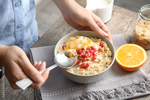 Woman eating quinoa porridge with nuts, orange and pomegranate seeds at table, closeup. Tasty breakfast