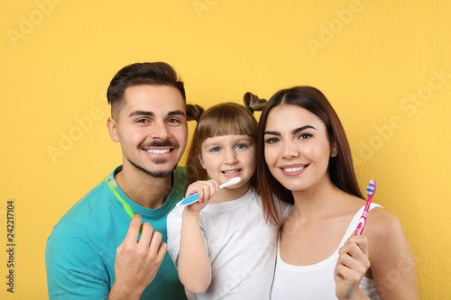 Little girl and her parents brushing teeth together on color background