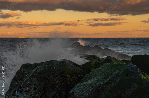 Beautiful golden sunset over the Jersey Shore featuring waves hitting the rocks on the foreground