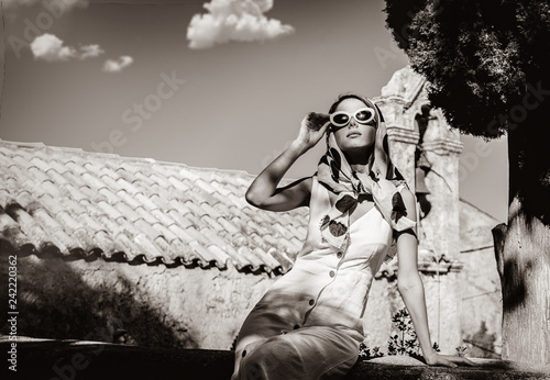 Young girl dressing in 60s style clothes in a village with old church on background. Crete, Greece