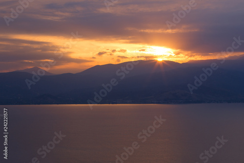 beautiful picturesque romantic sunset scenic landscape with sea calm water surface and vivid orange sun rays from above mountain ridge silhouette  post card landscape wallpaper pattern concept