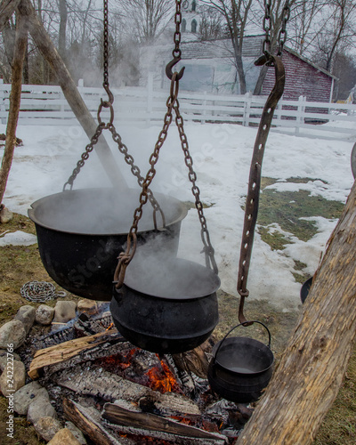 Maple sap boiling down in cauldrons over open fire