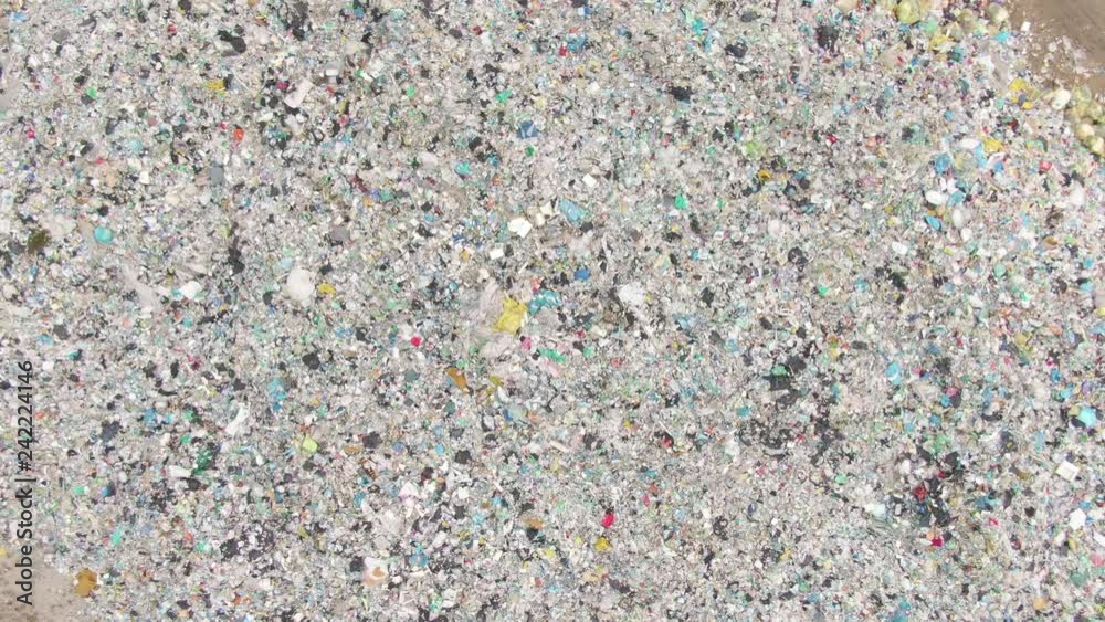 DRONE, TOP DOWN: Flying towards a huge stinky piles of scrap and plastic piling up in a big junkyard. Harmful waste an trash being collected in an industrial landfill. Large garbage disposal site.