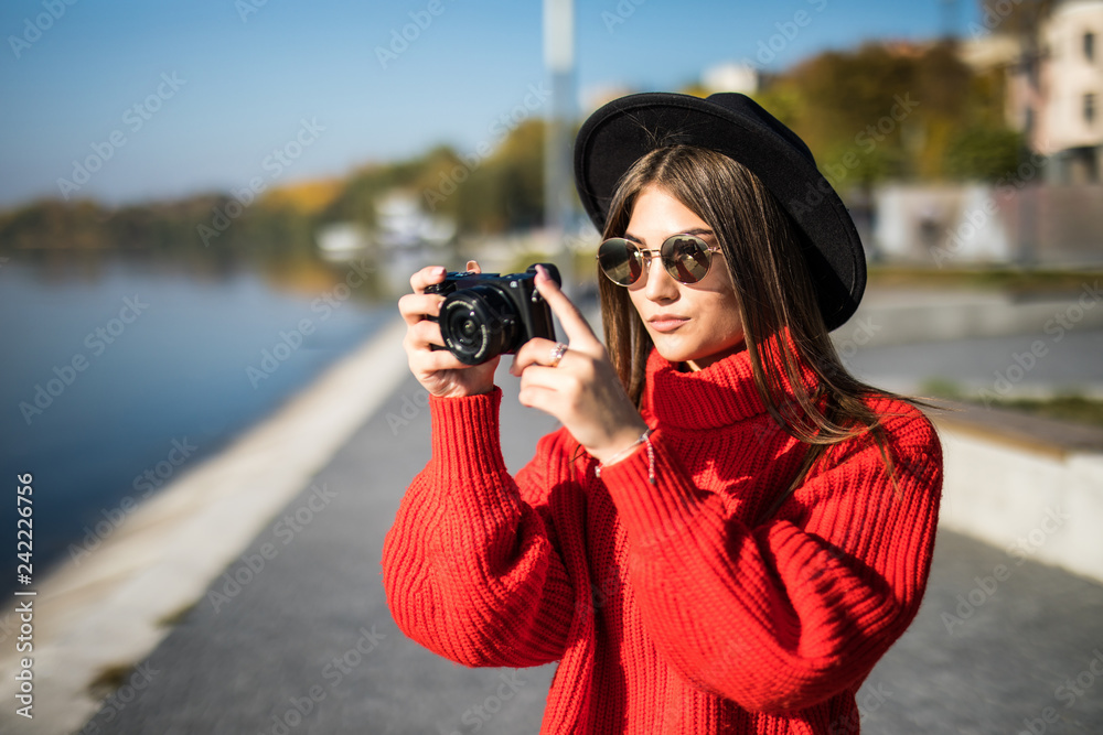 Young pretty woman in black hat and sunglasses taking photo with camera at city promenade pier. Young pretty woman in black hat and sunglasses taking photo with camera at city promenade pier.