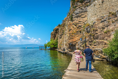 Ohrid, Macedonia - June 1st 2018 - Couple walking in a narrow wood path in front of a steep cliff in the edge of the amazing blue Ohrid lake in Macedonia © LMspencer