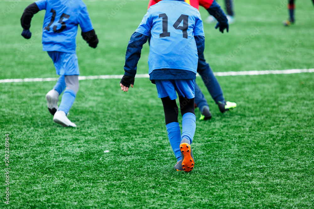 Boys in red and blue sportswear plays soccer on green grass field. Youth football game. Children sport competition, kids plays outdoor, winter activities, training Boys in red and blue sportswear plays soccer on green grass field. Youth football game. Children sport competition, kids plays outdoor, winter activities, training