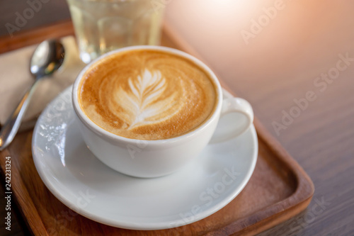 Hot latte art coffee in white cup with metal spoon on wooden table background