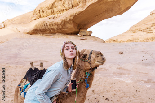 Young woman smiling posing with a camel in the middle of the jordan desert