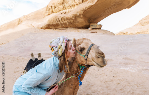 The woman touches with lips a muzzle of a camel in the Jordanian desert.