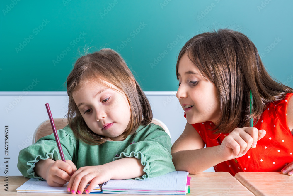 older sister looks at her younger sister as she draws in a notebook older sister looks at her younger sister as she draws in a notebook