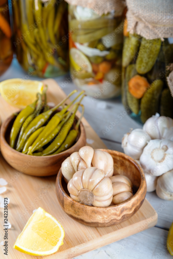 Bowl of pickled garlics and green peppers with jars of pickled vegetables on wooden background Bowl of pickled garlics and green peppers with jars of pickled vegetables on wooden background