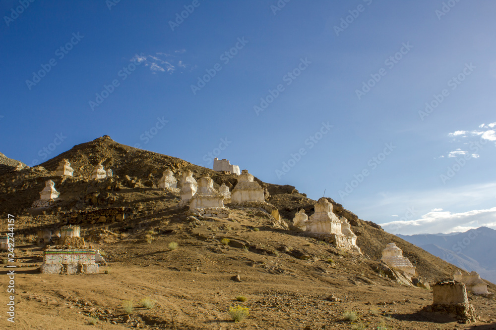 ancient white Tibetan Buddhist temples stupas on the slope of a desert hill against the blue sky and mountain valley