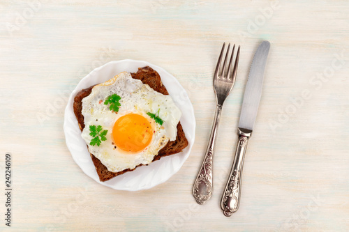 An overhead photo of an egg cooked sunny side up on a toast with a fork, knife and copy space