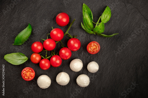 Mozzarella cheese, cherry tomatoes and fresh basil leaves, shot from the top on a black background, Italian cuisine ingredients with a place for text