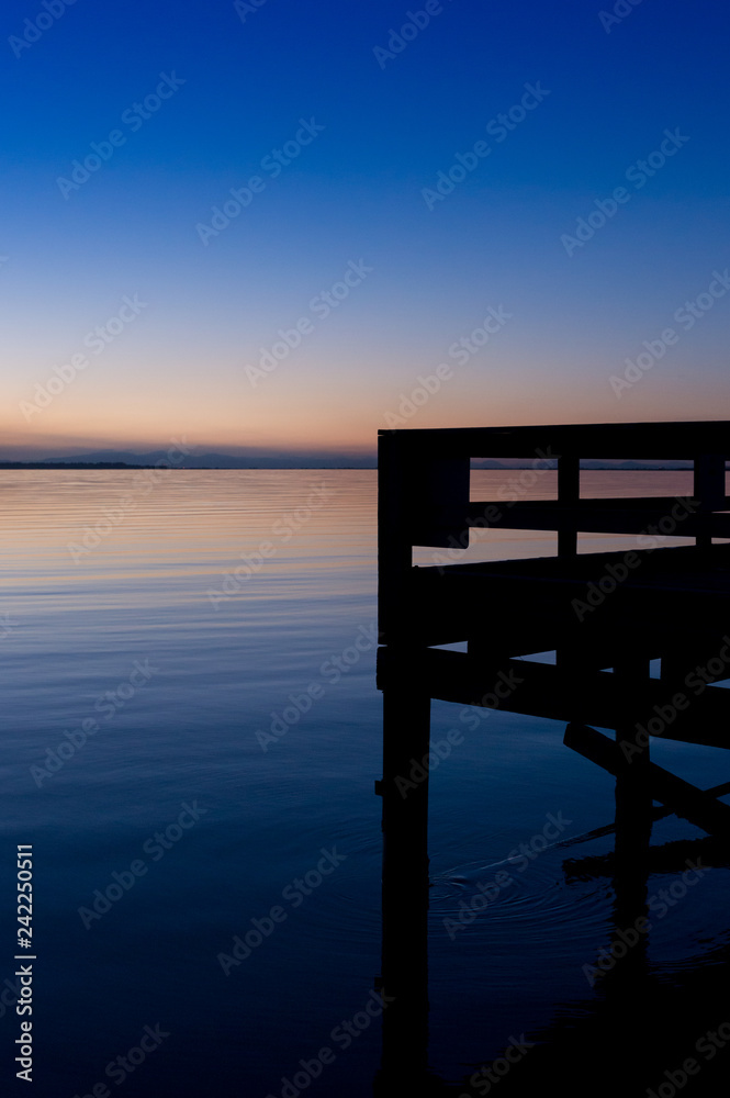 Silhouette of pier overlooking calm ocean bay in the blue hour of dusk.