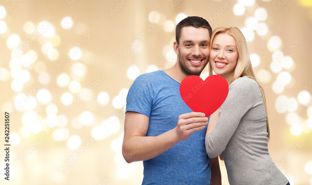 love, valentines day and charity concept - happy couple with big red heart over beige background and festive lights