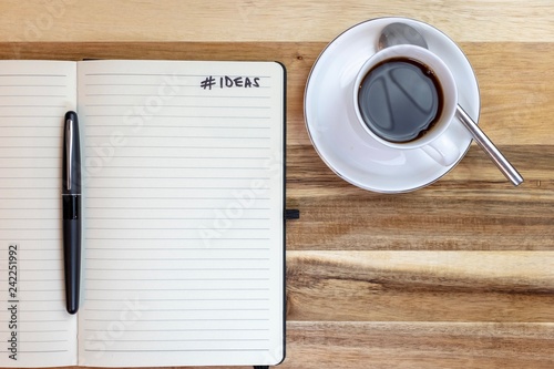 Ideas journal with pen and a black coffee on attractive wooden background 