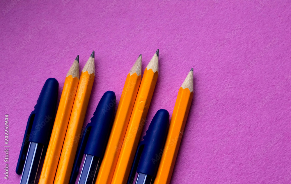 A group of simple orange pencils with blue pens close-up on a pink background A group of simple orange pencils with blue pens close-up on a pink background