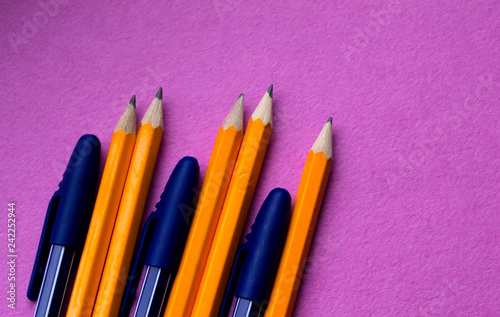 A group of simple orange pencils with blue pens close-up on a pink background