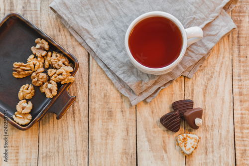 Cup of hot black tea with chocolate candy and walnuts on wooden table. Flat lay, top view.