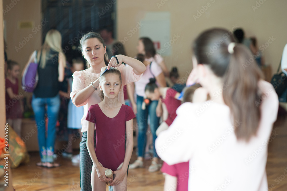 Fototapeta premium young caucasian mother corrects her ballerina dancer little slim daughter's hair before concert show