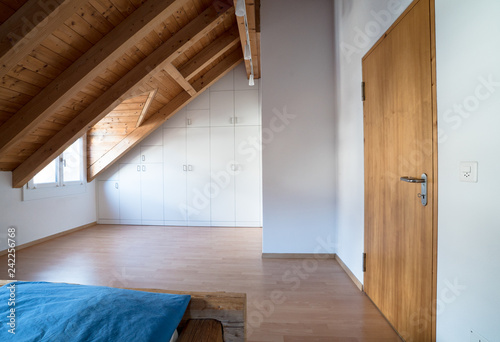 bright light modern simple master bedroom with wooden parquet floors and designer closet and traditional wooden beam bed under slanted ceiling in a refurbished apartment