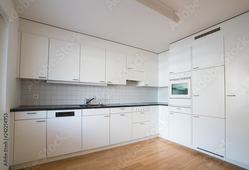 modern bright kitchen in an empty refurbished apartment with black granite work surface and wooden parquet floor