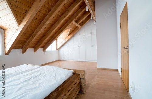 bright light modern simple master bedroom with wooden parquet floors and designer closet and traditional wooden beam bed under slanted ceiling in a refurbished apartment