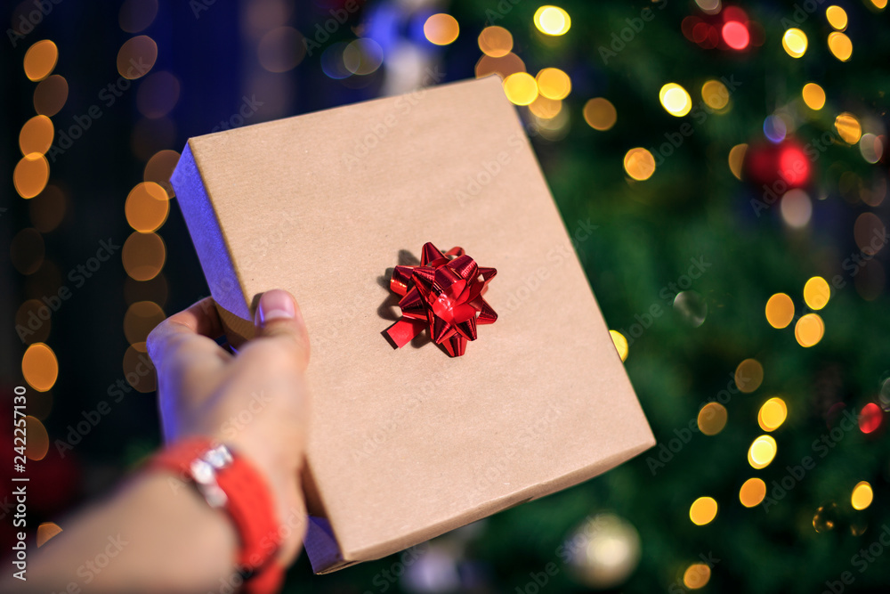 Hand with a gift box near the fir tree Hand with a gift box near the fir tree