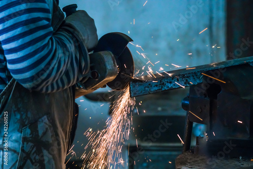 Working man with angle grinder, process of cutting carbonated steel metal with quantity of sparks in workshop