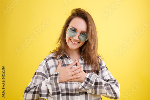 Positive beautiful young woman in blue glasses and a plaid shirt is smiling leaning her arms to the chest. Advertising space © Rithor
